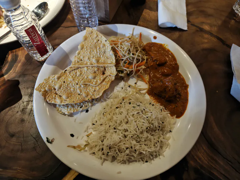 A close-up plate with papdi chaat-style papdis, biryani, rice, and curry on a rustic wooden table.